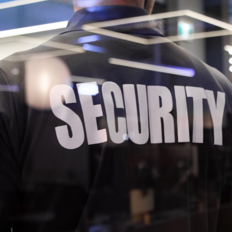 A security guard standing inside a commercial building nearby the window reflecting light.